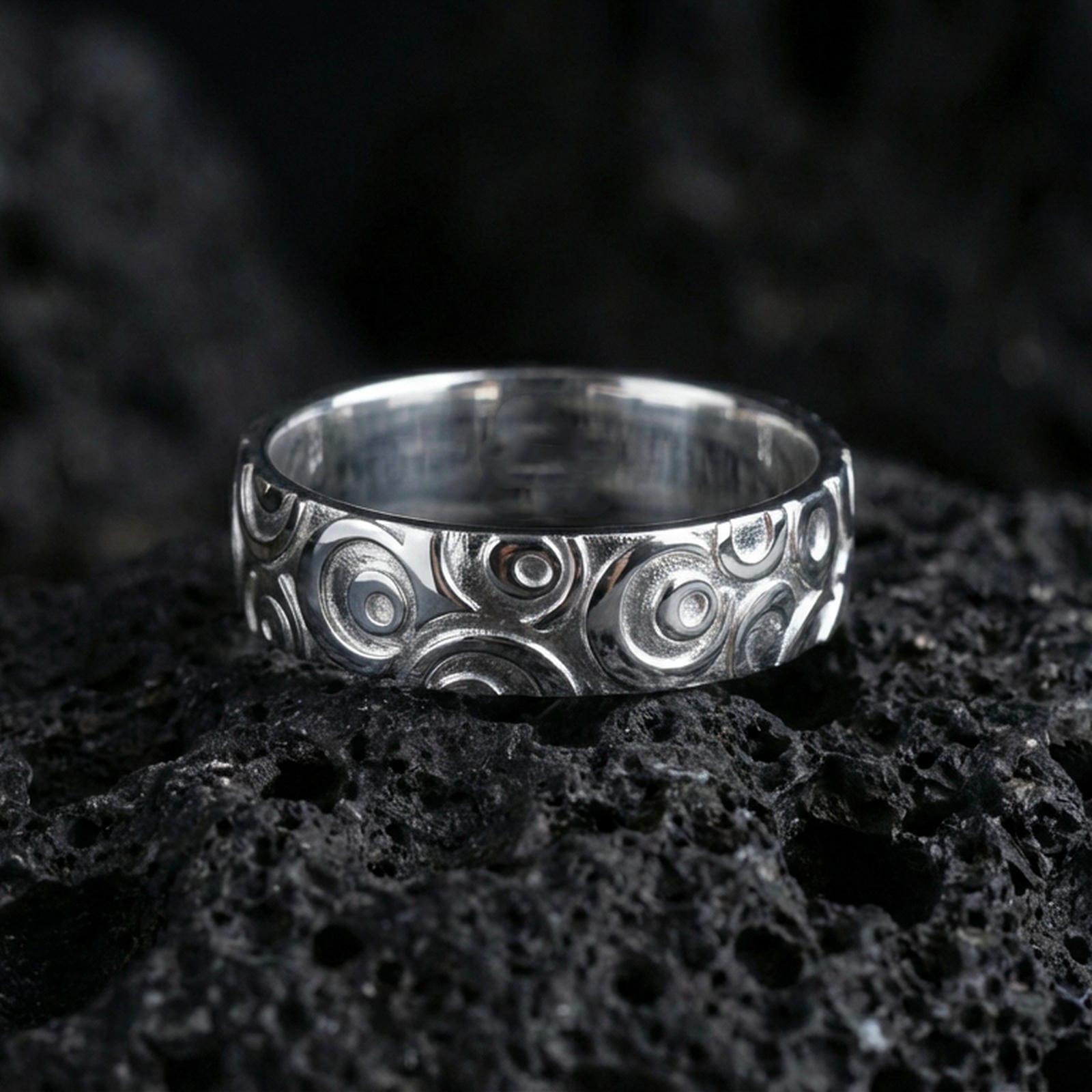 Polished silver geometric circle pattern ring on volcanic stone, clean product shot emphasizing smooth shine and crisp circular engraving depth.