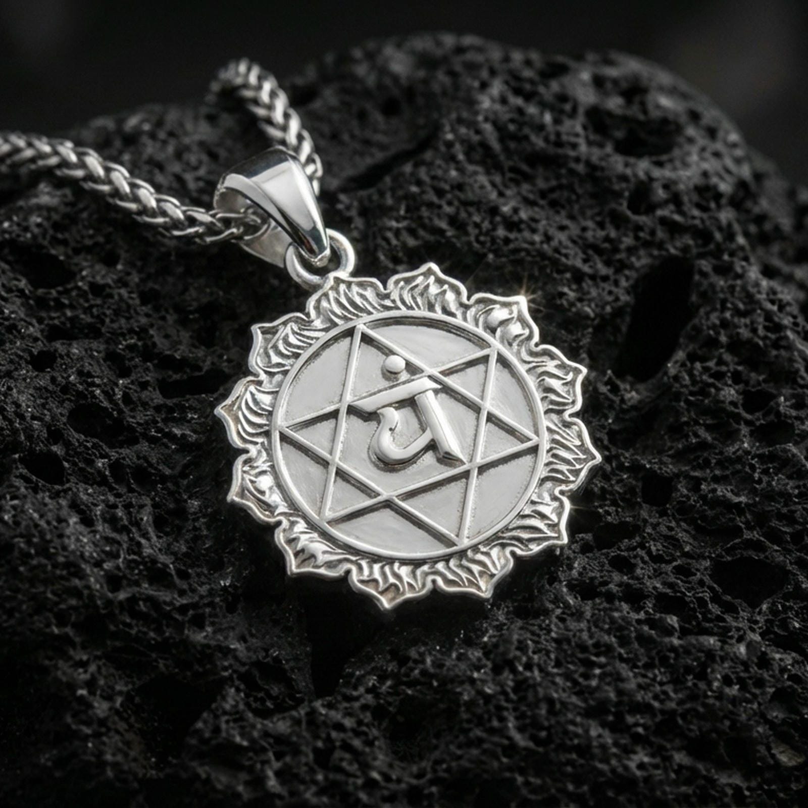 Polished silver heart chakra necklace with raised Anahata symbol, geometric star design, and detailed circular frame placed on textured volcanic rock in a premium studio product shot