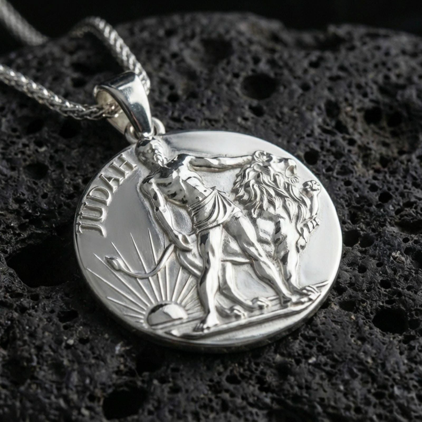 Polished silver Lion of Judah medallion with circular coin design, standing lion relief, and Judah lettering placed on textured volcanic rock in a premium studio product shot