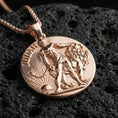 Load image into Gallery viewer, Rose gold plated Lion of Judah pendant with circular coin silhouette, lion relief, and engraved Judah inscription resting on volcanic rock in an elegant close-up product presentation
