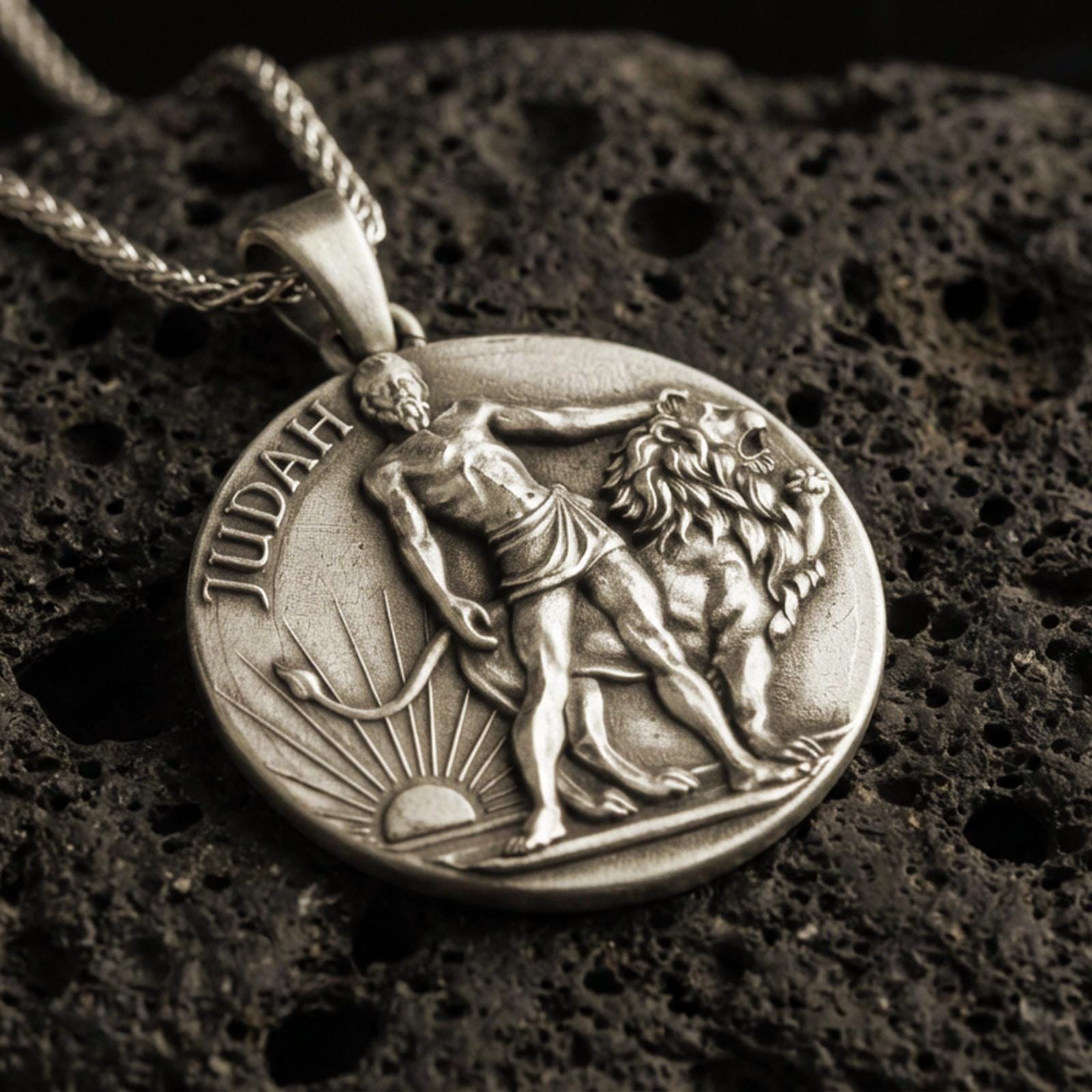 Bronze Lion of Judah pendant with Judah inscription, lion figure, and sunrise motif displayed on dark volcanic rock in a close-up luxury jewelry composition