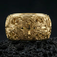 Load image into Gallery viewer, Gold plated ornate cross band ring on volcanic stone, premium close-up showcasing warm gold tone across the raised cross and flowing filigree texture.

