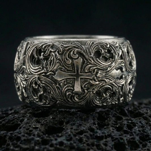 Oxidized sterling silver ornate cross band ring on volcanic stone, macro close-up highlighting deep relief scrollwork and antique contrast around the cross motif.