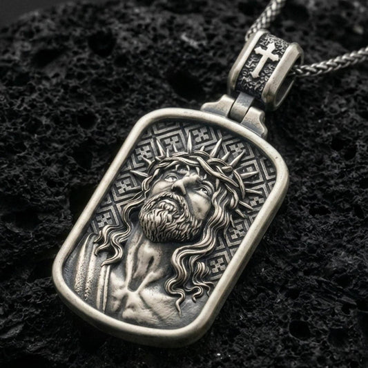 Oxidized Jesus Christ pendant with crown of thorns, framed sacred portrait, and detailed devotional relief displayed on dark volcanic rock in a close-up luxury jewelry composition