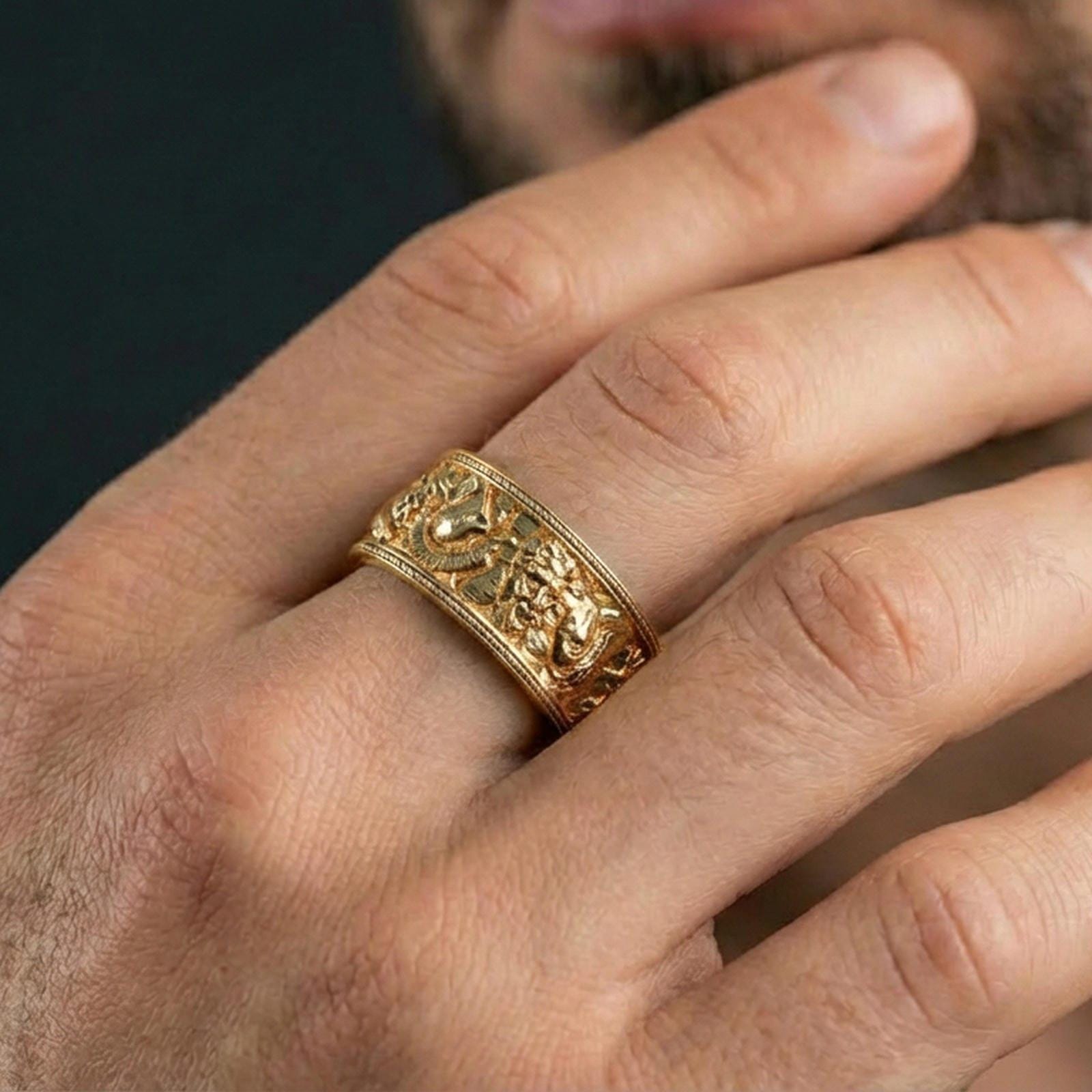 Gold plated mythic faces cuff band ring worn on a finger, lifestyle wear photo emphasizing luxurious gold tone and sculptural character relief.