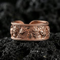 Load image into Gallery viewer, Rose gold plated mythic faces cuff band ring on volcanic stone, refined macro shot capturing soft rose highlights on the relief faces and border rope detailing.

