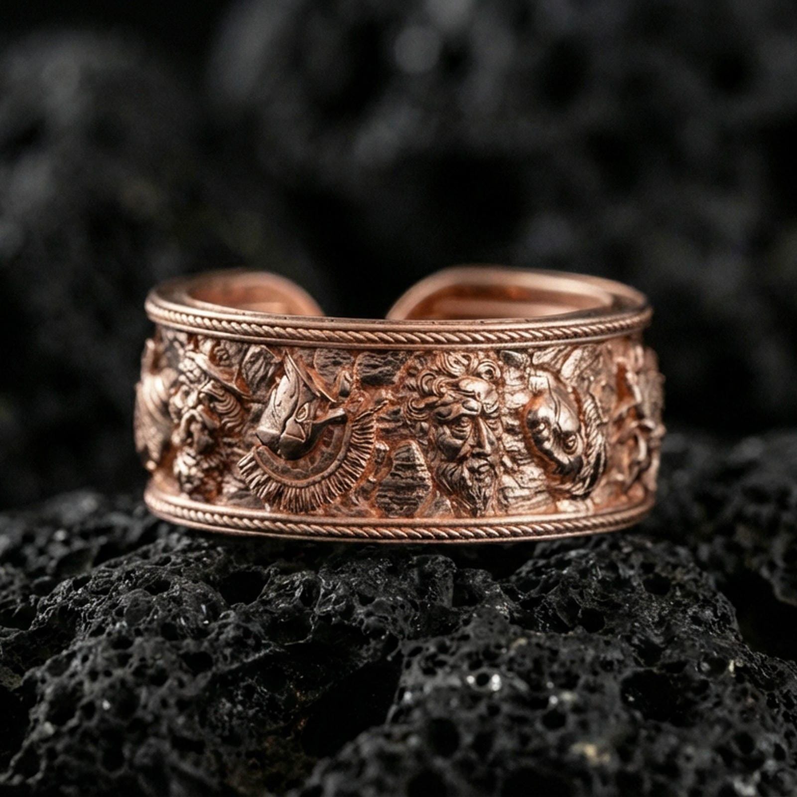Rose gold plated mythic faces cuff band ring on volcanic stone, refined macro shot capturing soft rose highlights on the relief faces and border rope detailing.