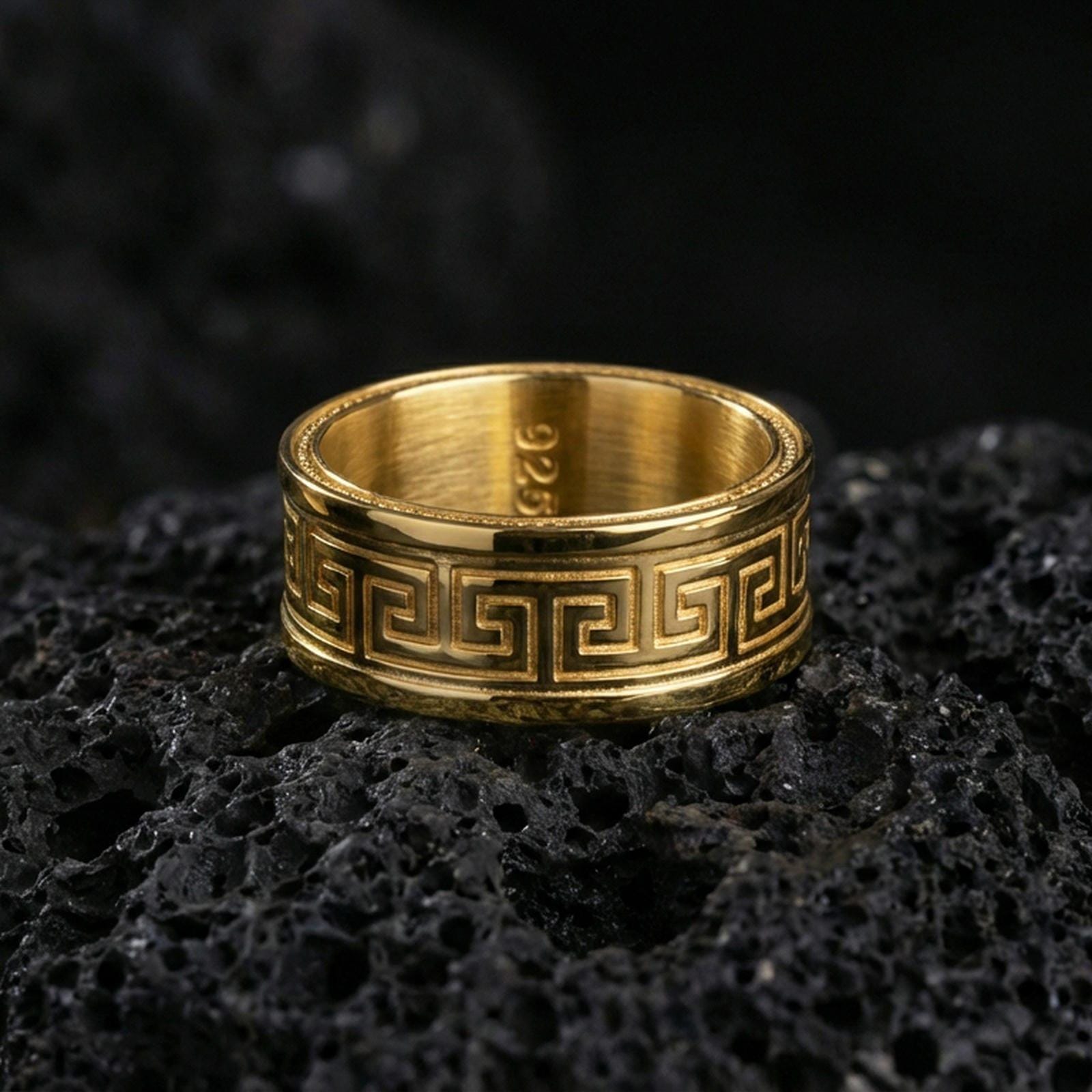Gold plated Greek key spinner ring on volcanic stone, premium close-up emphasizing warm gold tone along the meander design and refined engraved contrast.
