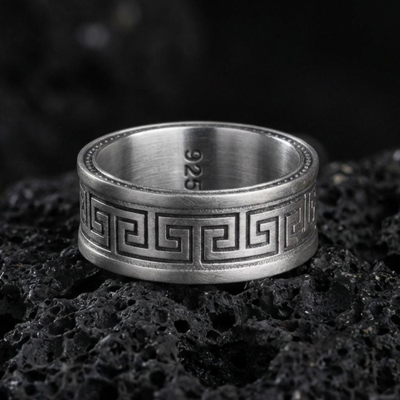 Oxidized sterling silver Greek key spinner ring on volcanic stone, macro close-up highlighting darkened recesses, crisp meander lines, and antique depth.