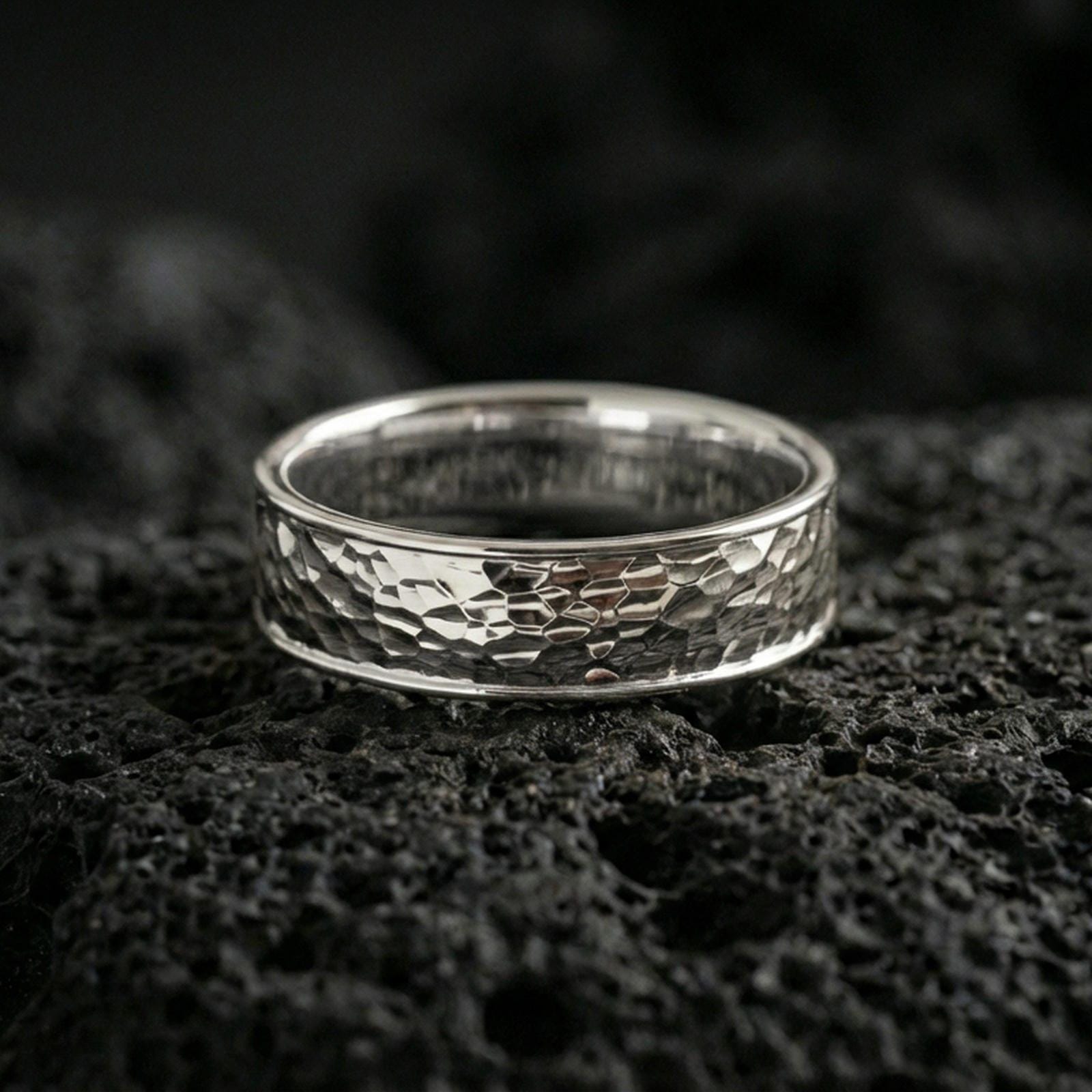 Polished silver hammered texture band ring on volcanic stone, clean studio macro highlighting crisp hammered pattern, bright reflections, and smooth comfort edges.