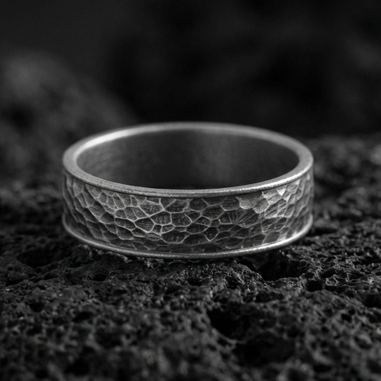 Oxidized sterling silver hammered texture band ring on volcanic stone, macro close-up showcasing deepened recesses, rugged facets, and antique character.