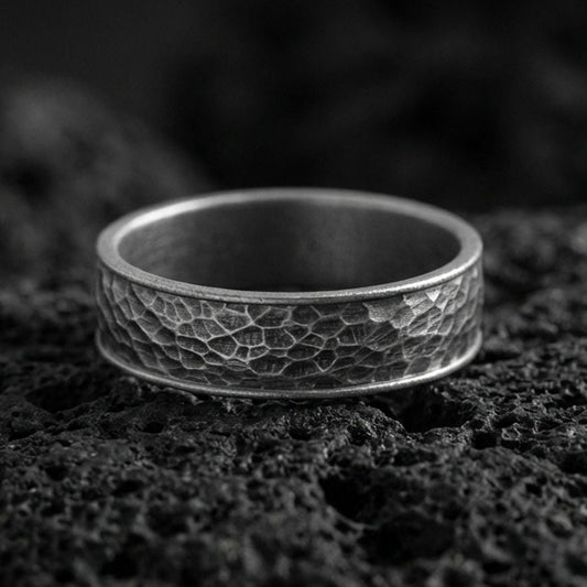 Oxidized sterling silver hammered texture band ring on volcanic stone, macro close-up showcasing deepened recesses, rugged facets, and antique character.