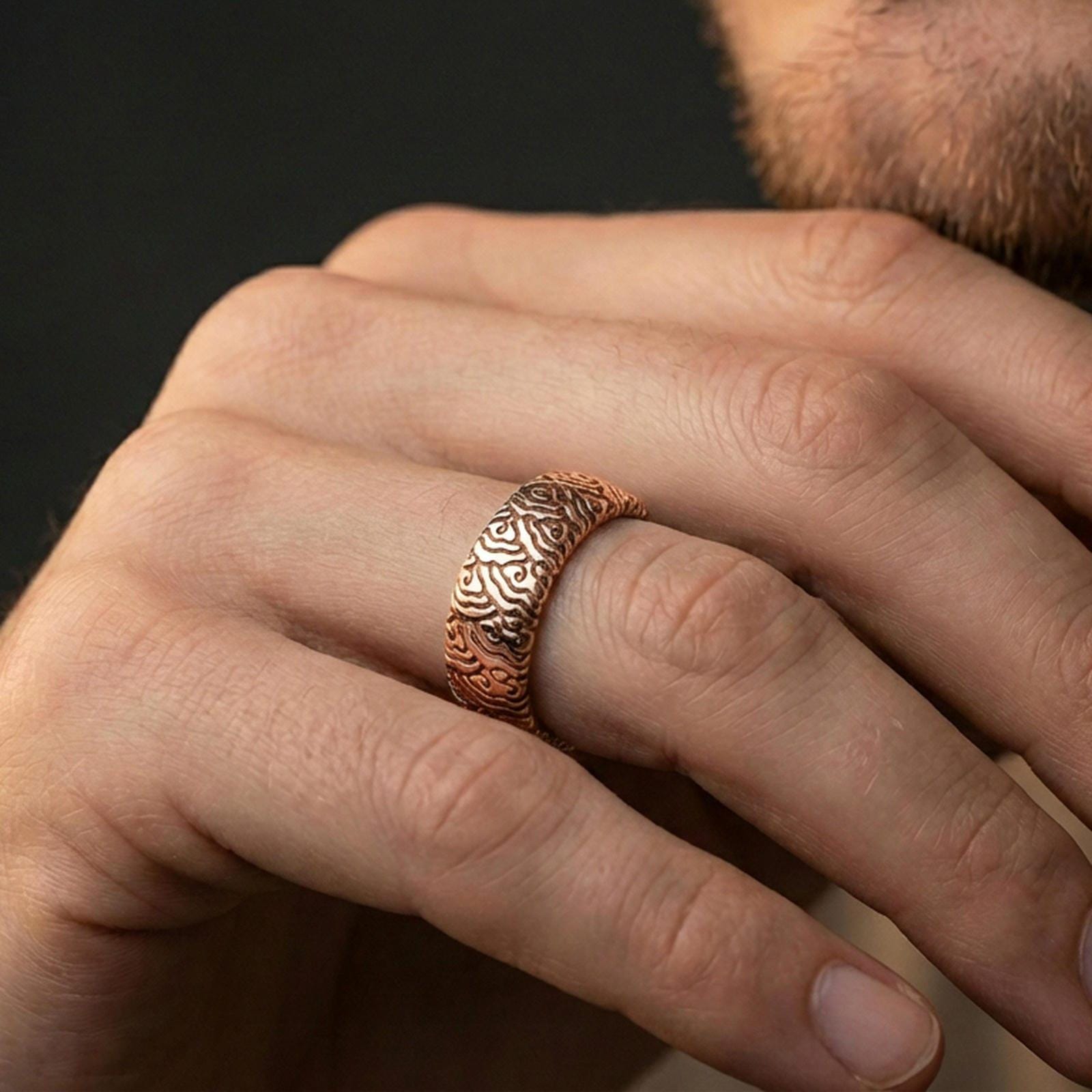 Rose gold plated wave pattern band ring worn on a finger, lifestyle image showcasing warm rose tone, flowing wave engraving, and refined modern aesthetic.