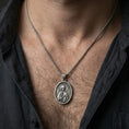 Load image into Gallery viewer, Oxidized Saint Anastasia pendant with haloed saint figure worn on the neck in a lifestyle jewelry shot, styled against the chest for a devotional and timeless look
