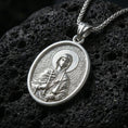 Load image into Gallery viewer, Polished silver Saint Anastasia medallion with engraved orthodox saint relief, halo motif, and oval frame placed on textured volcanic rock in a premium studio product shot
