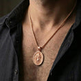 Load image into Gallery viewer, Rose gold plated Saint Paul pendant with haloed portrait and oval medal form worn on the neck in a refined lifestyle shot with a warm and elegant presentation
