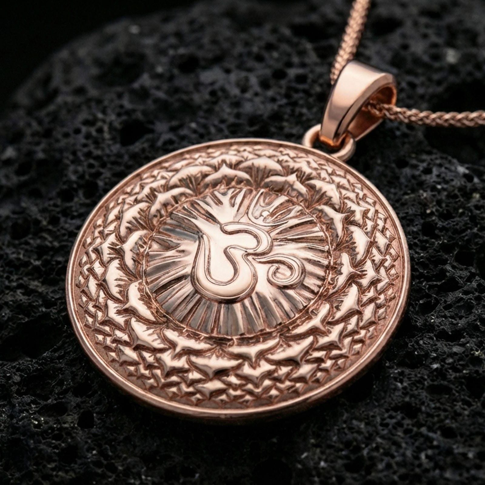 Rose gold plated spiritual medallion with centered Om motif, mandala-inspired patterning, and elegant round silhouette resting on volcanic rock in an elegant close-up product presentation