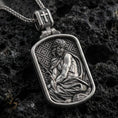 Load image into Gallery viewer, Oxidized Jesus Christ pendant with seated sacred figure, crown of thorns, and framed devotional relief displayed on dark volcanic rock in a close-up luxury jewelry composition
