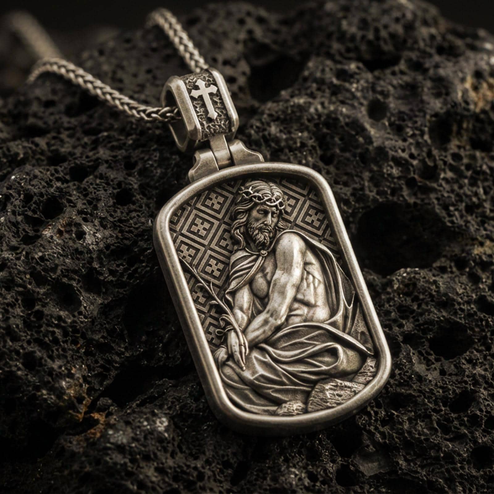 Bronze Jesus Christ pendant with seated sacred figure, crown of thorns, and framed devotional relief displayed on dark volcanic rock in a close-up luxury jewelry composition