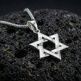 Load image into Gallery viewer, Polished silver Star of David necklace with clean angular structure, layered six-pointed star design, and minimalist symbolic form placed on textured volcanic rock in a premium studio product shot
