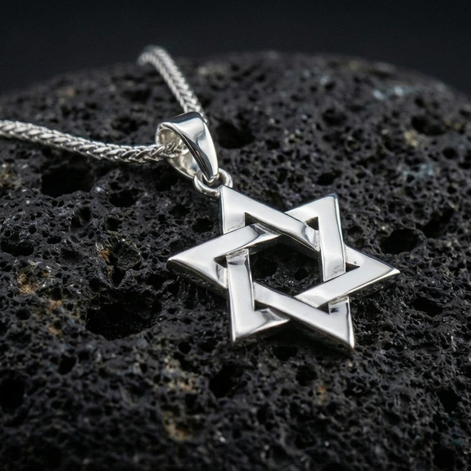 Polished silver Star of David necklace with clean angular structure, layered six-pointed star design, and minimalist symbolic form placed on textured volcanic rock in a premium studio product shot
