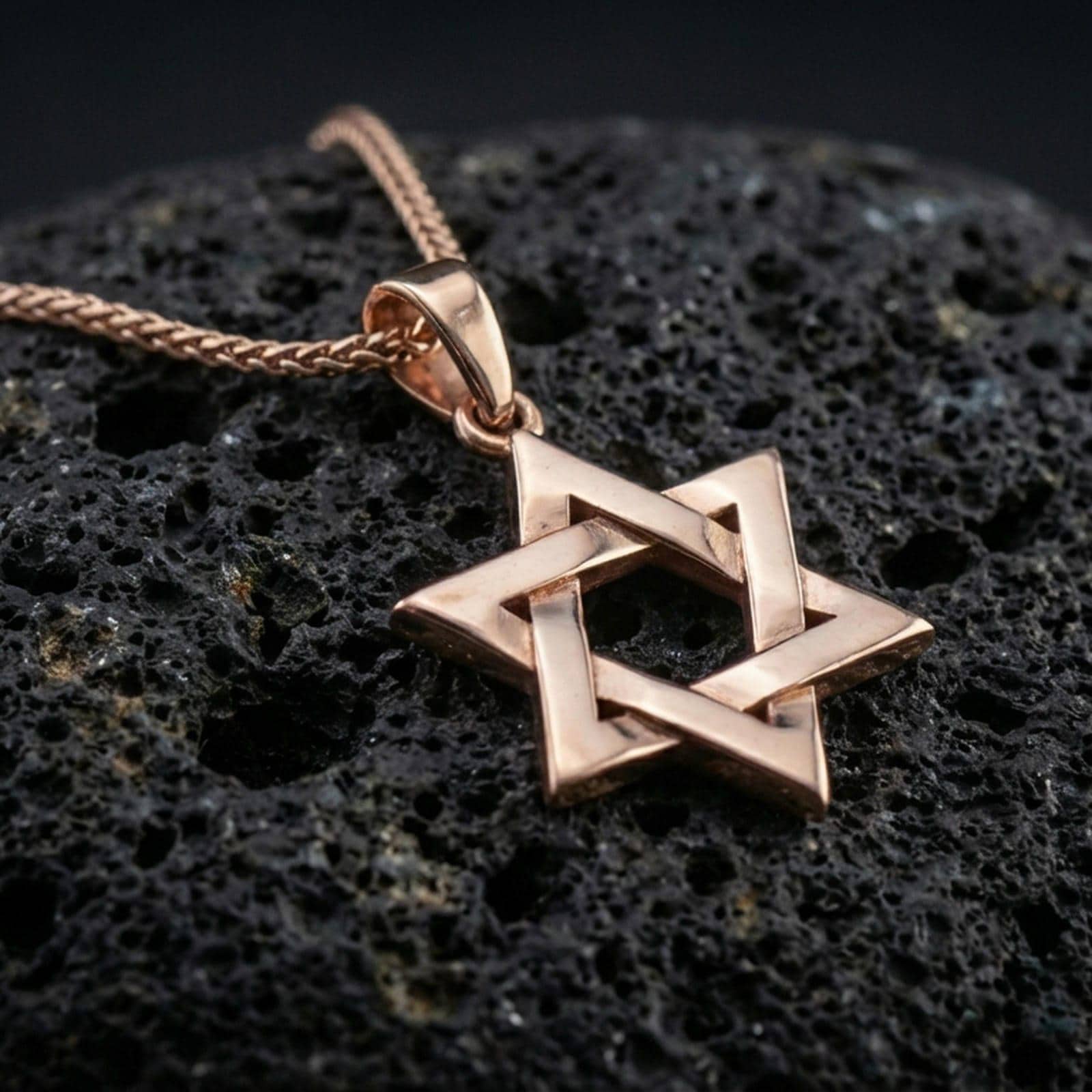 Rose gold plated Star of David necklace with open six-pointed star form, polished geometric relief, and timeless symbolic design resting on volcanic rock in an elegant close-up product presentation