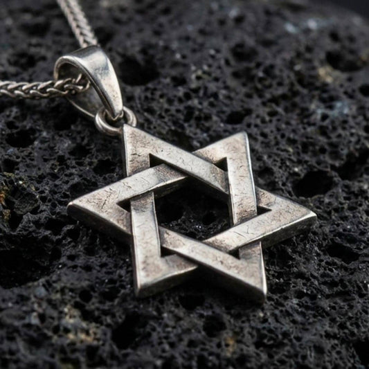 Oxidized Star of David pendant with interlocking geometric lines and open hexagram silhouette displayed on dark volcanic rock in a close-up luxury jewelry composition