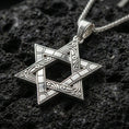Load image into Gallery viewer, Polished silver Star of David necklace with interlocking six-pointed star design, decorative engraved details, and refined symbolic structure placed on textured volcanic rock in a premium studio product shot
