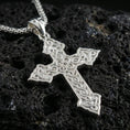 Load image into Gallery viewer, Polished silver cross necklace with detailed interwoven Celtic pattern, pointed cross ends, and refined openwork design placed on textured volcanic rock in a premium studio product shot
