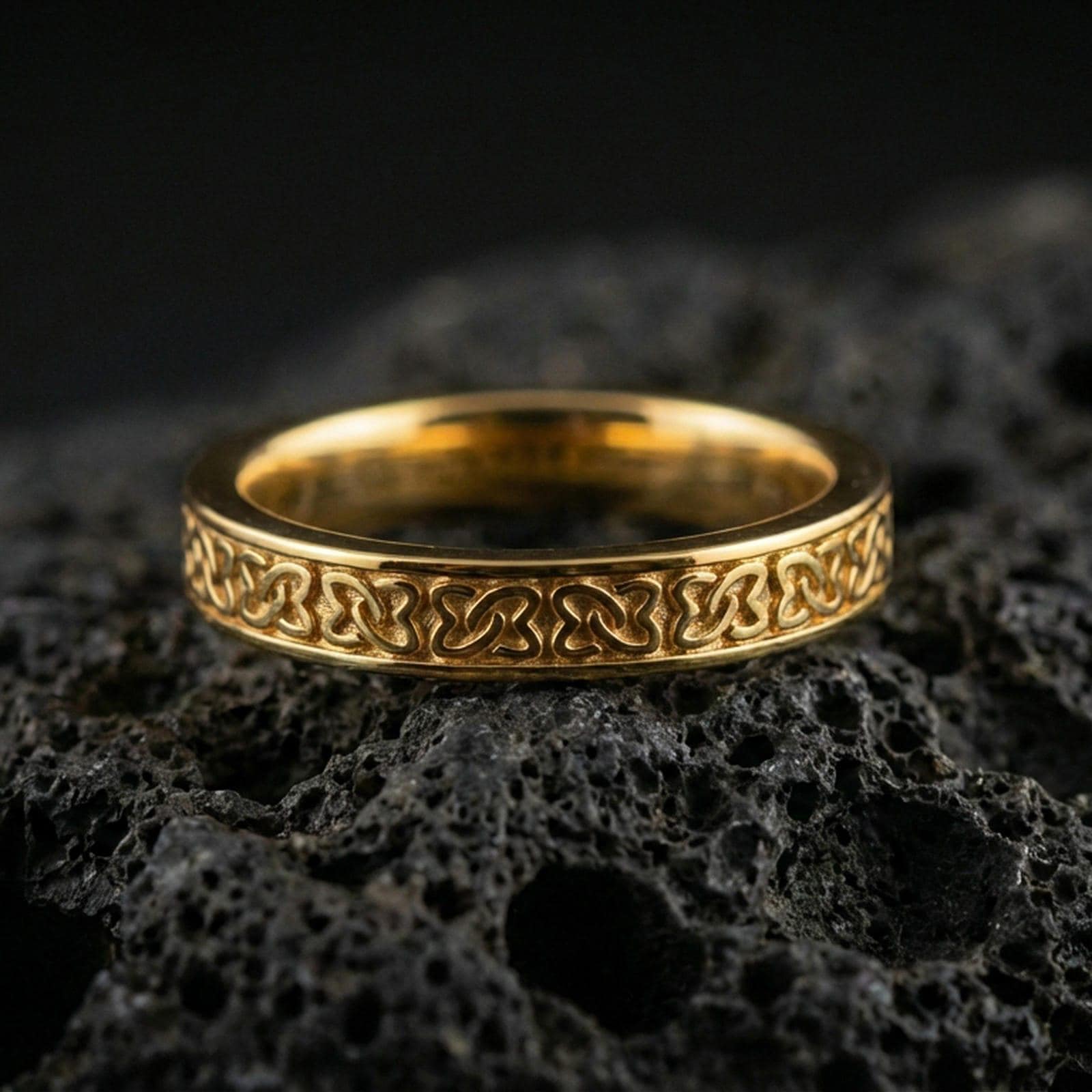 Gold plated Celtic knot band ring on volcanic stone, premium macro close-up showcasing warm gold tone across the continuous interlace design.