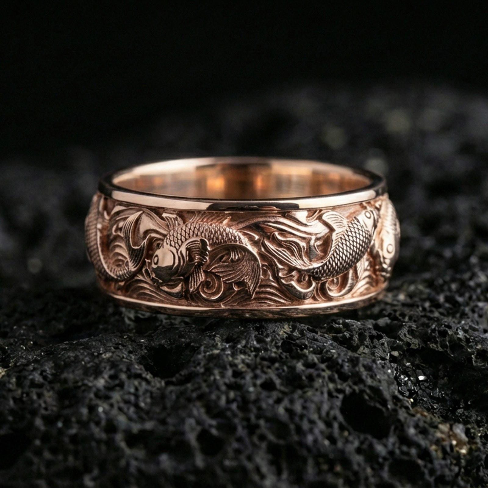 Rose gold plated koi fish band ring on volcanic stone, elegant macro close-up capturing soft rose reflections across the koi and wave detailing.