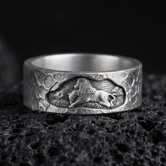 Oxidized sterling silver lion band ring on volcanic stone, macro close-up highlighting the carved lion relief, hammered texture, and deep shadow contrast.