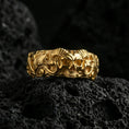 Load image into Gallery viewer, Gold plated skull ring on volcanic stone, premium macro shot capturing warm gold tone on the horned skull centerpiece and sculpted filigree sides.
