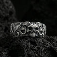 Load image into Gallery viewer, Oxidized sterling silver skull ring on volcanic stone, macro close-up highlighting horned skull relief, deep blackened recesses, and ornate scrollwork.
