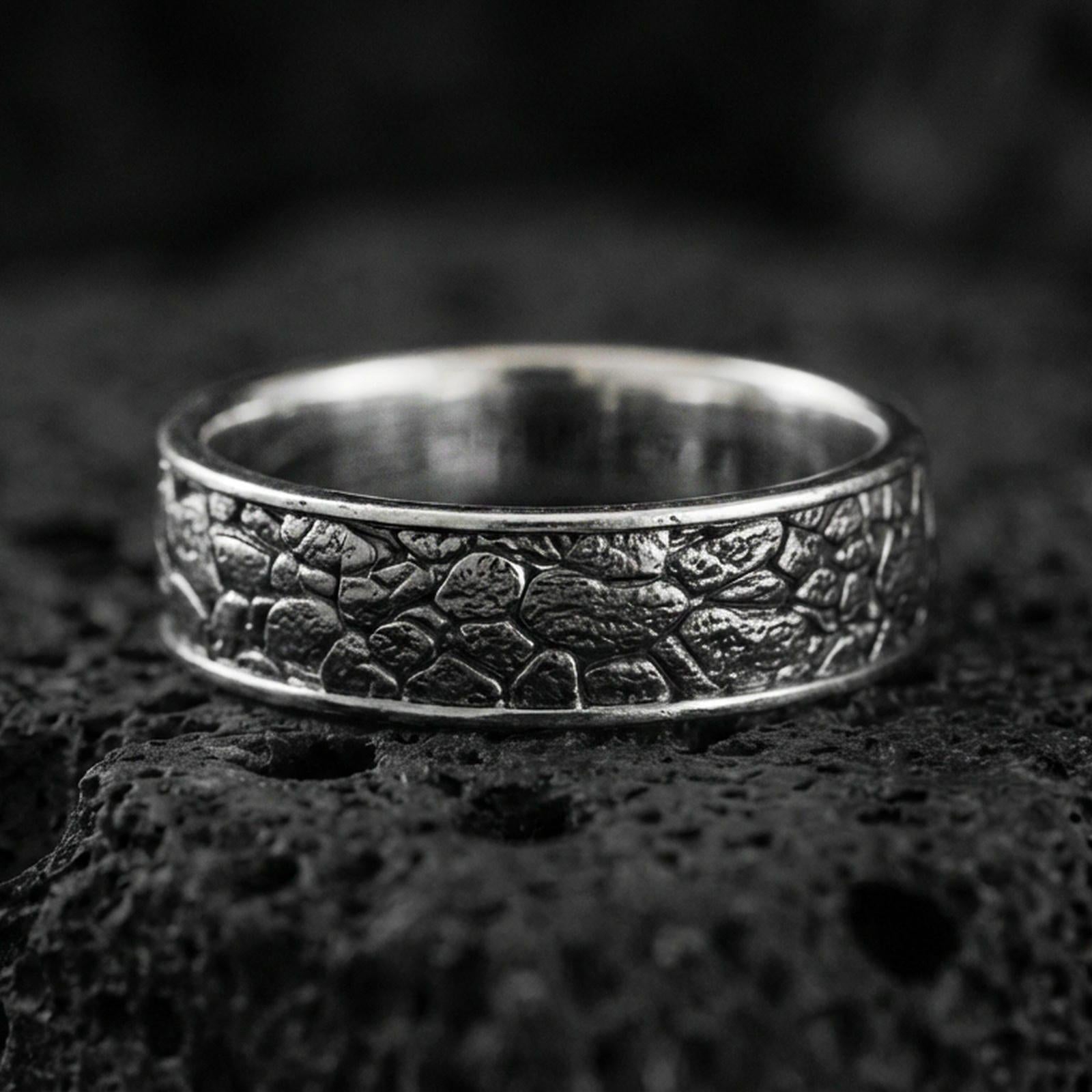 Oxidized sterling silver pebble texture band ring on volcanic stone, macro close-up highlighting hammered stone-like relief and darkened depth.