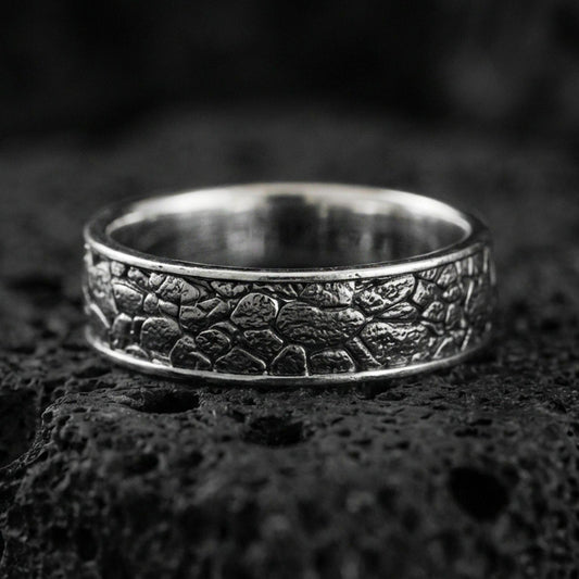 Oxidized sterling silver pebble texture band ring on volcanic stone, macro close-up highlighting hammered stone-like relief and darkened depth.