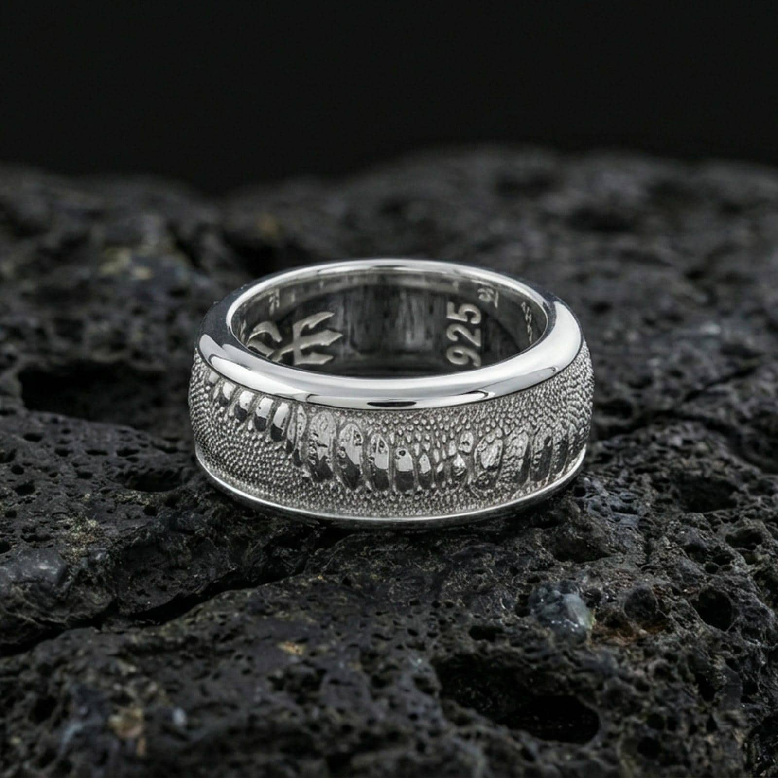 Polished silver lizard skin spinner ring on volcanic stone, sharp macro photo emphasizing bright shine, smooth edges, and crisp scale detailing on the spinning center.