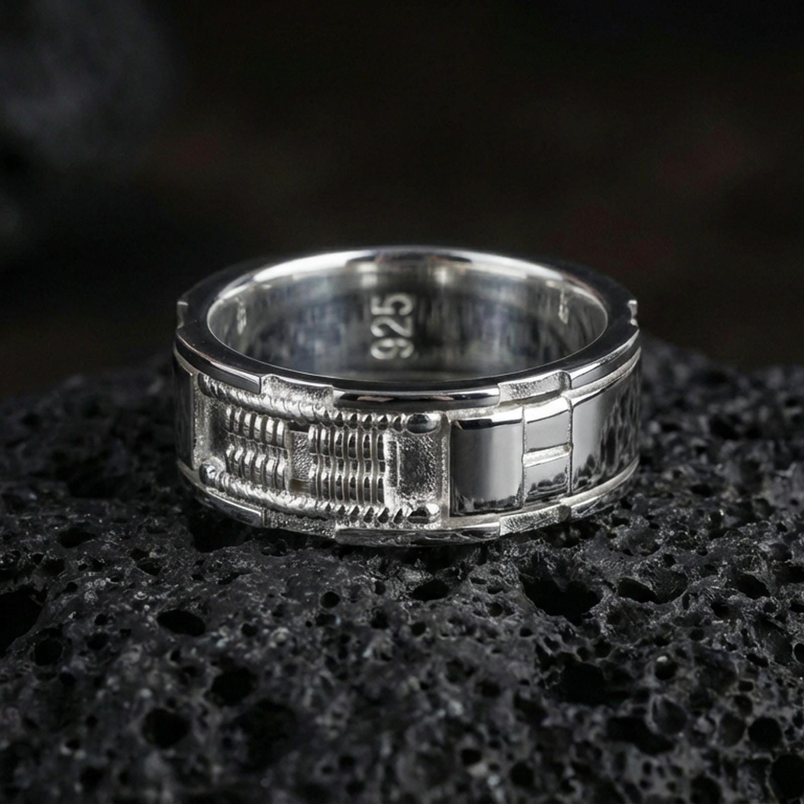 Polished silver sci-fi band ring on volcanic stone, sharp macro photo emphasizing crisp edges, clean shine, and the layered mechanical pattern.