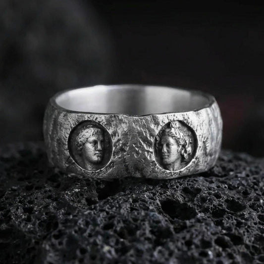 Oxidized sterling silver Greek sculpture ring on volcanic stone, macro close-up focusing on the twin cameo portraits, deep shadowing, and rugged antique patina.