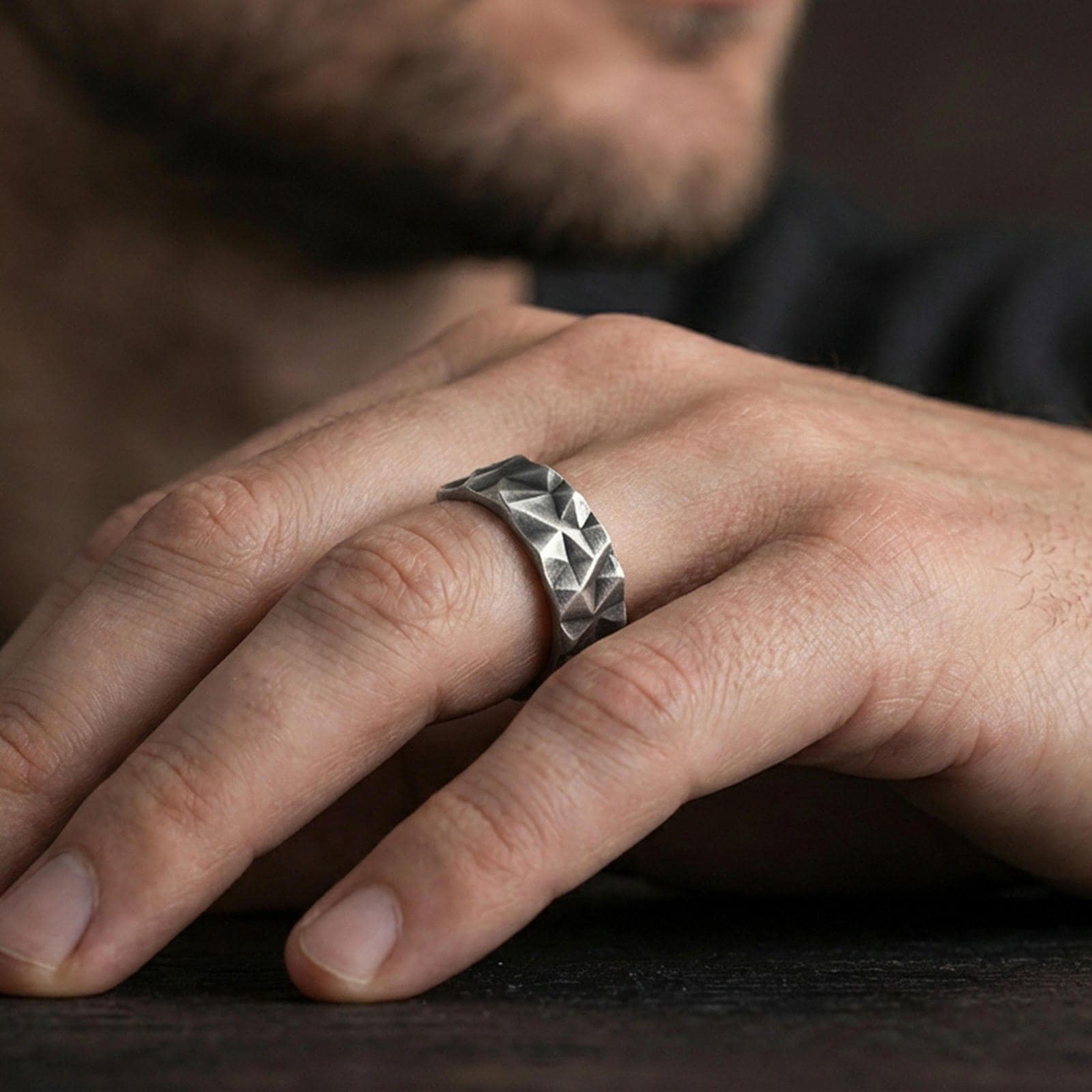 Oxidized sterling silver faceted geometric band ring worn on the finger, lifestyle image showing bold modern texture and rugged statement look.