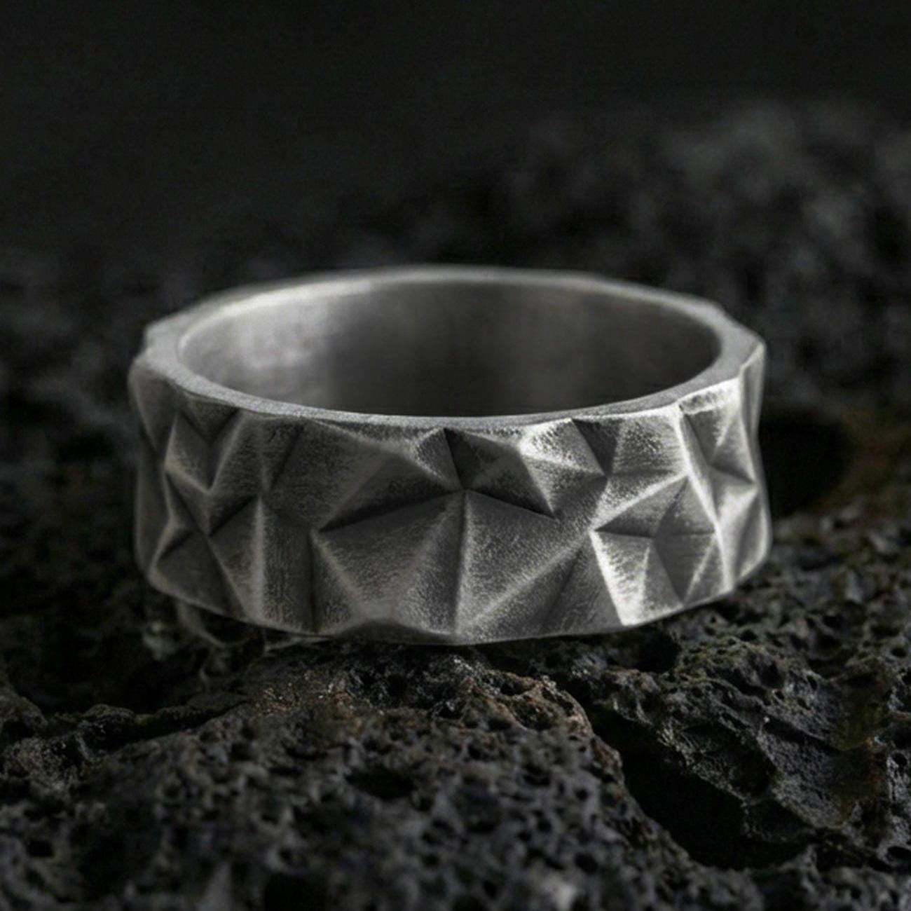 Oxidized sterling silver faceted geometric band ring on volcanic stone, macro close-up highlighting sharp pyramid cuts and deep contrast shadows.