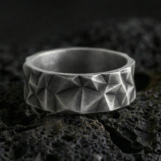 Oxidized sterling silver faceted geometric band ring on volcanic stone, macro close-up highlighting sharp pyramid cuts and deep contrast shadows.
