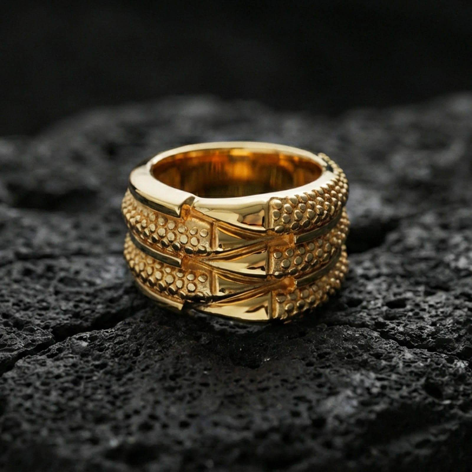 Gold plated layered studded band ring on volcanic stone, luxury macro photo showcasing warm gold tone across the rivet-like dots and sculpted band layers.