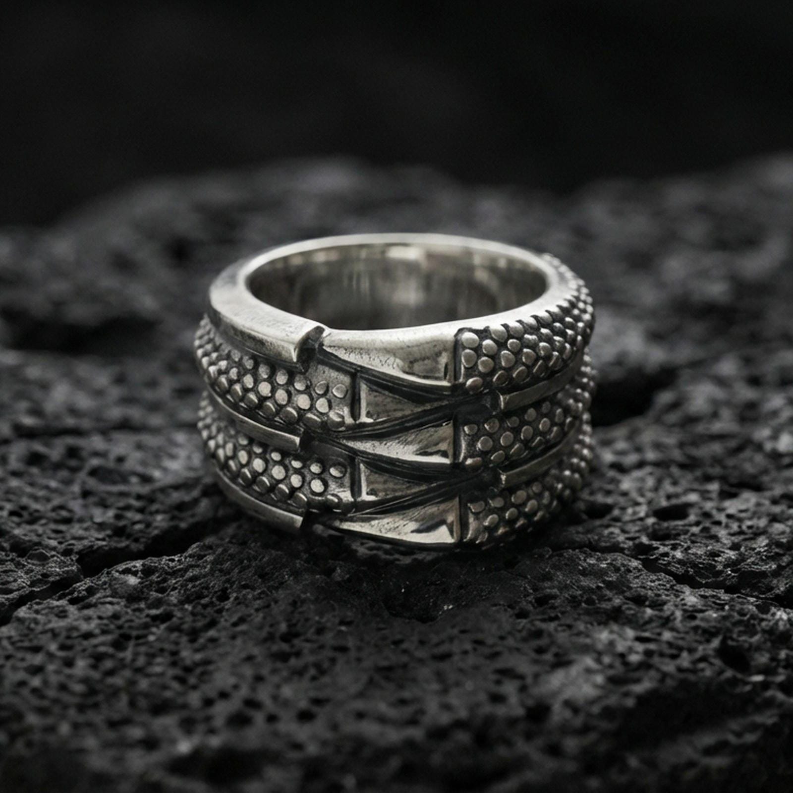 Oxidized sterling silver layered studded band ring on volcanic stone, macro close-up highlighting dotted texture panels and bold industrial ridge lines.