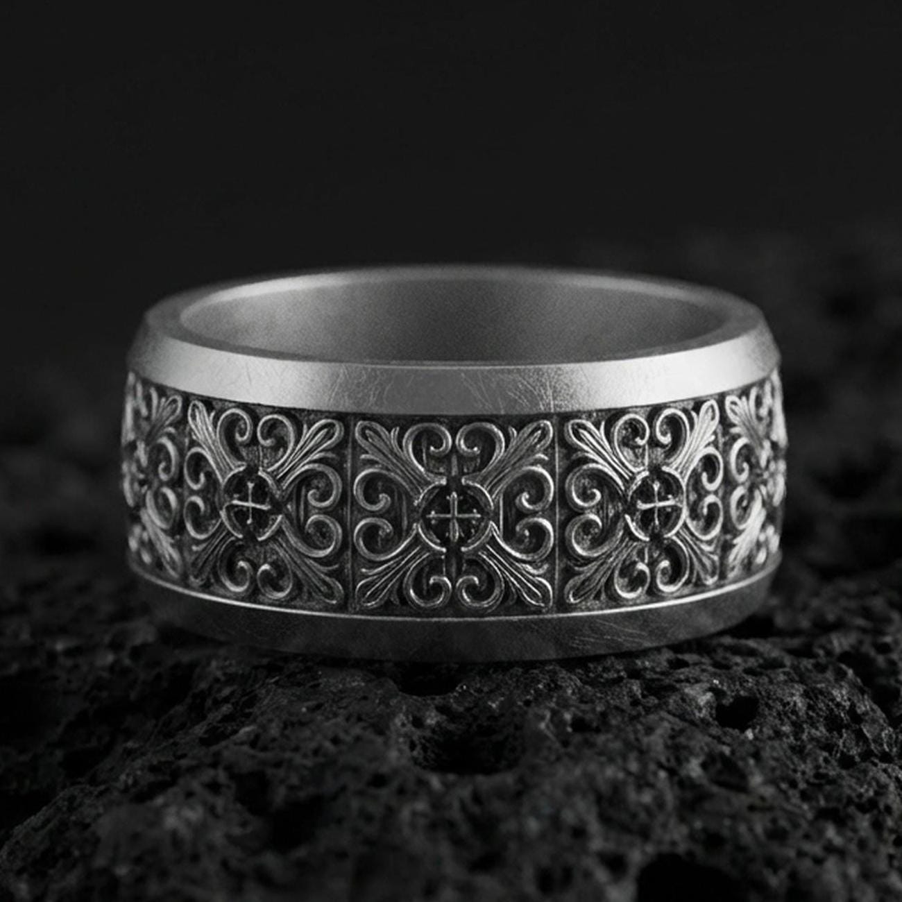 Oxidized sterling silver cross scrollwork band ring on volcanic stone, macro close-up showing deep darkened recesses and ornate vintage filigree detail.