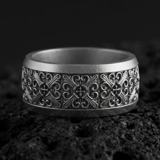 Oxidized sterling silver cross scrollwork band ring on volcanic stone, macro close-up showing deep darkened recesses and ornate vintage filigree detail.