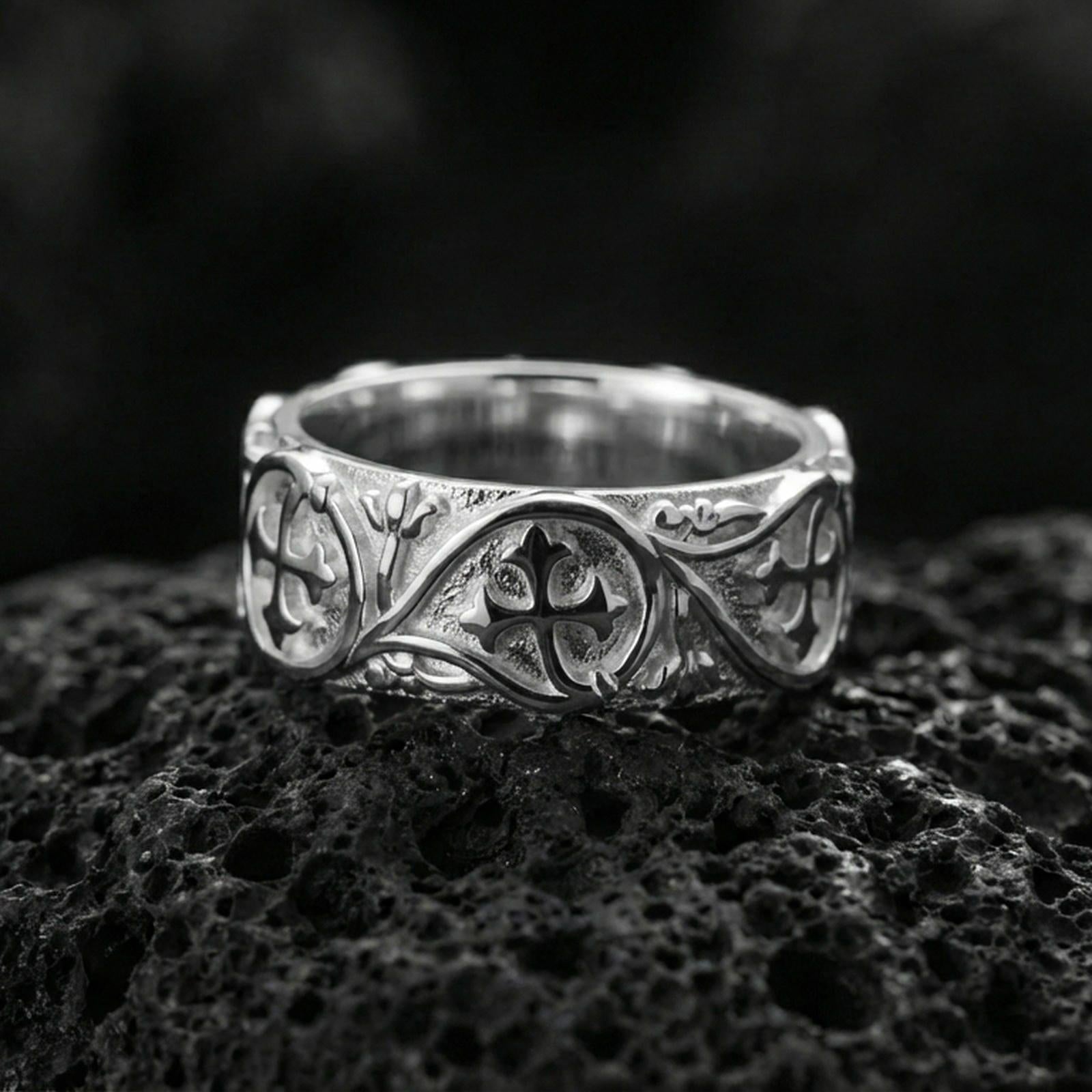 Polished silver quatrefoil cross band ring on volcanic stone, crisp macro photo highlighting bright shine, clean edges, and symmetrical scrollwork framing.