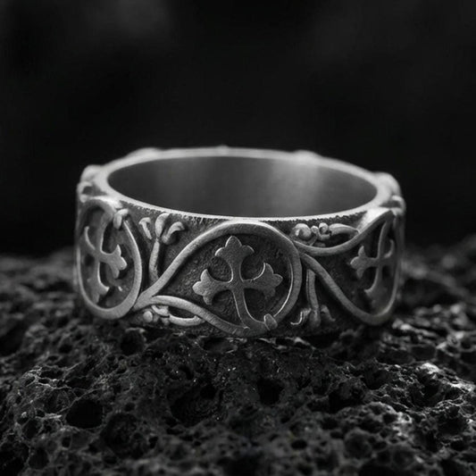 Oxidized sterling silver quatrefoil cross band ring on volcanic stone, macro close-up showing darkened recessed background and raised cross medallion details.