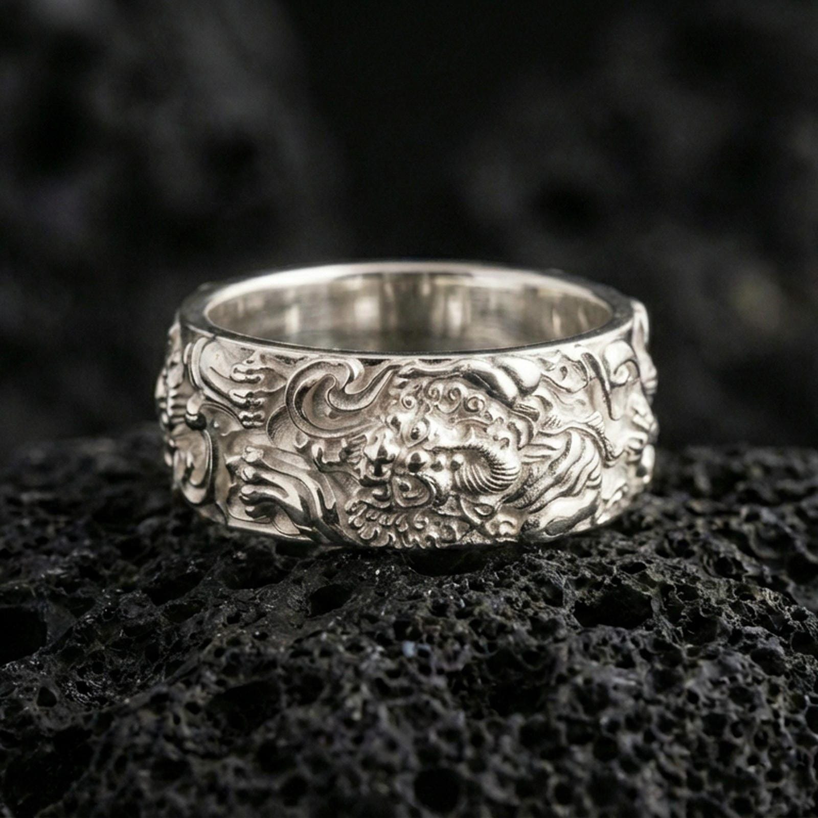 Polished silver guardian lion band ring on volcanic stone, crisp macro photo emphasizing bright reflective edges, sculpted mane texture, and clean ornamental scrollwork.