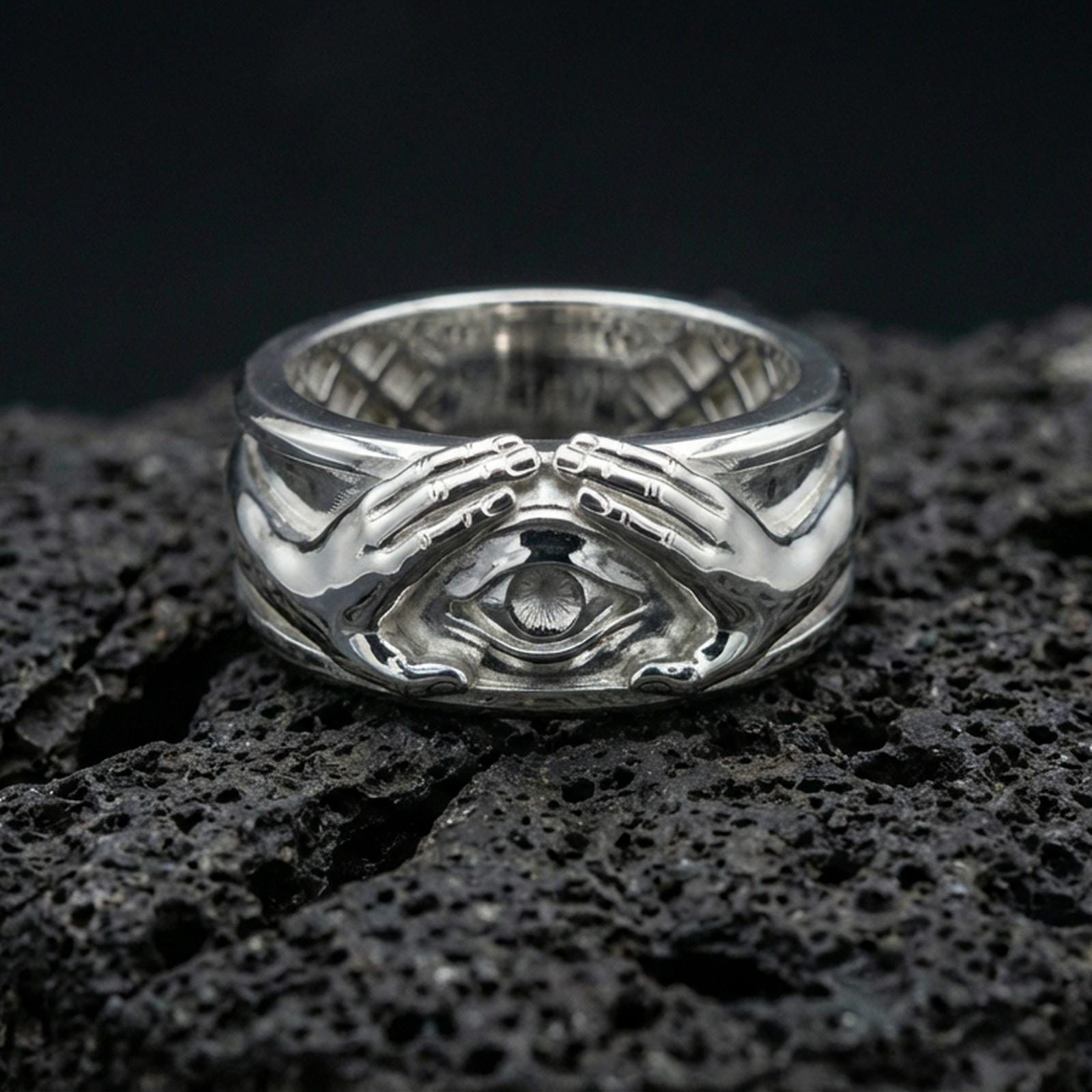 Polished silver protective eye ring on volcanic stone, crisp macro shot emphasizing smooth reflective edges, clean hand contours, and defined iris detail.